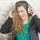 Smiling woman with curly hair wearing headphones and a black jacket over a green top.