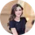 Smiling woman with shoulder-length brown hair wearing a black top in a softly lit indoor setting.